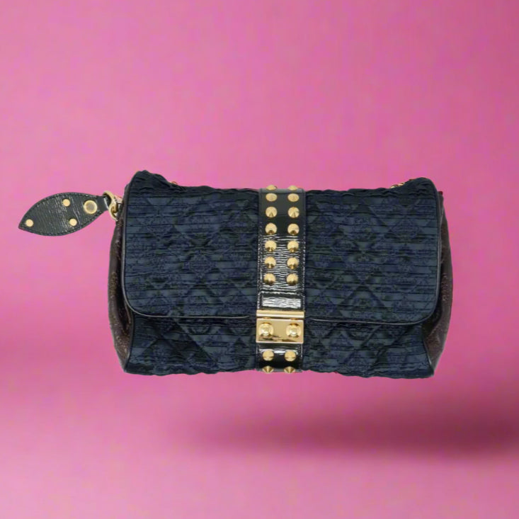 Black quilted handbag with gold studs on a pink background