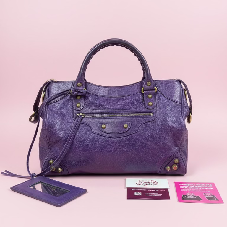 Purple handbag with gold accents held by a hand, with a blurred background of other bags.