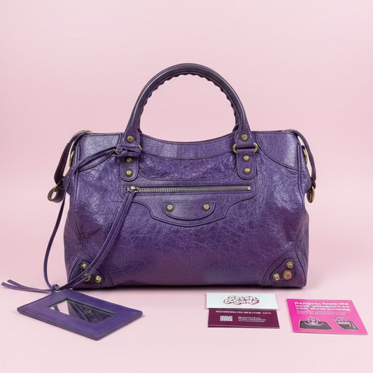 Purple handbag with gold accents held by a hand, with a blurred background of other bags.