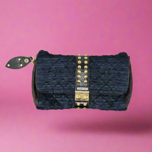 Black quilted handbag with gold studs on a pink background