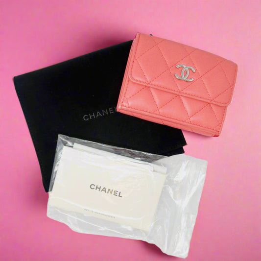 Pink quilted Chanel wallet with black and white packaging on a light gray background