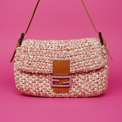Pink woven handbag with brown leather accents on a pink background