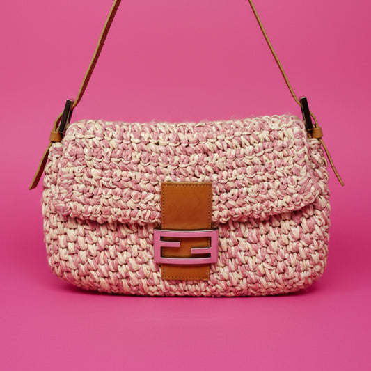 Pink woven handbag with brown leather accents on a pink background